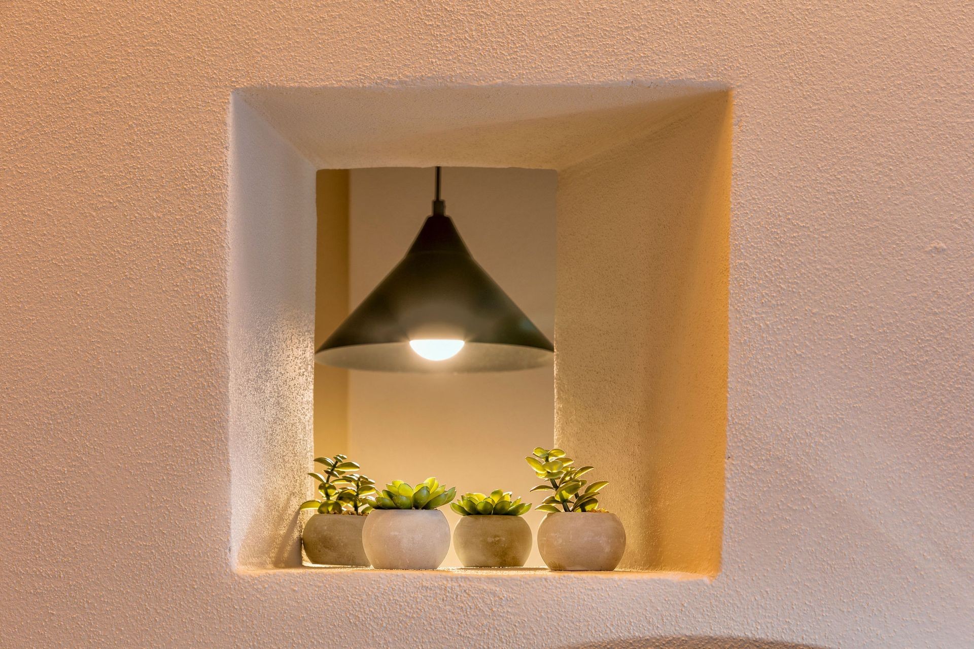 Wall niche with hanging lamp and small potted succulents on display.